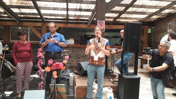 Un intervenant en chemise bleue, accompagné d'une participante en tenue bordeaux, écoute un musicien en chemise imprimée jouant sur scène lors de la remise des prix LanKRéol 2017. Des instruments de musique et des équipements audio sont visibles en arrière-plan.