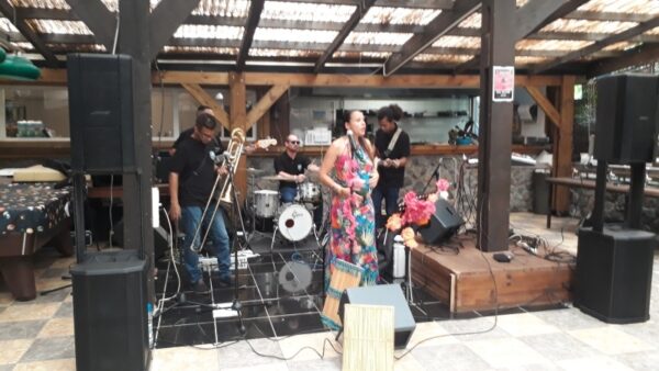 Le groupe musical est réuni sur la scène lors de la remise des prix LanKRéol 2017. Une chanteuse au centre, habillée d'une robe colorée, chante au micro, tandis que le tromboniste et les autres musiciens sont à leurs postes derrière elle