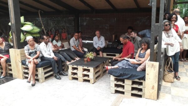 Un groupe d'invités est assis sur des sièges en bois autour de petites tables lors de la remise des prix LanKRéol 2017. Certains discutent, d'autres observent la scène en arrière-plan, tandis que d'autres profitent d'un moment de détente."