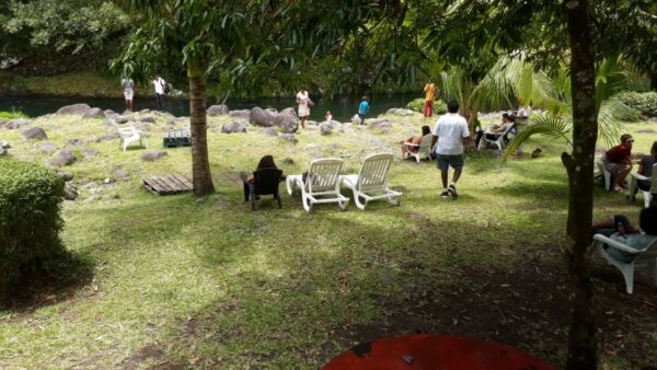 Un espace de détente en plein air est aménagé avec des tables, des chaises blanches et des transats lors de la remise des prix LanKRéol 2017. Des invités se promènent et discutent à l'ombre des arbres dans une ambiance conviviale