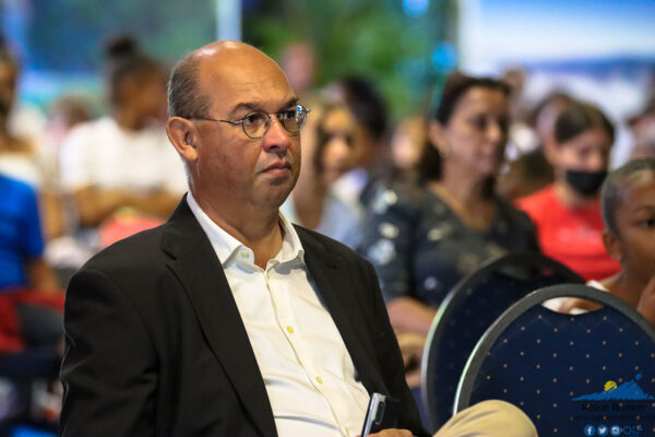 Michael maillot directeur du CCEE en costume écoute attentivement lors d'un événement public, avec d'autres participants en arrière-plan.