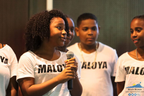 Une jeune fille du groupe Maloya s'exprimant avec un micro lors d'un événement.