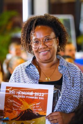 Une femme souriante tenant une affiche du Pri Honoré 2022.