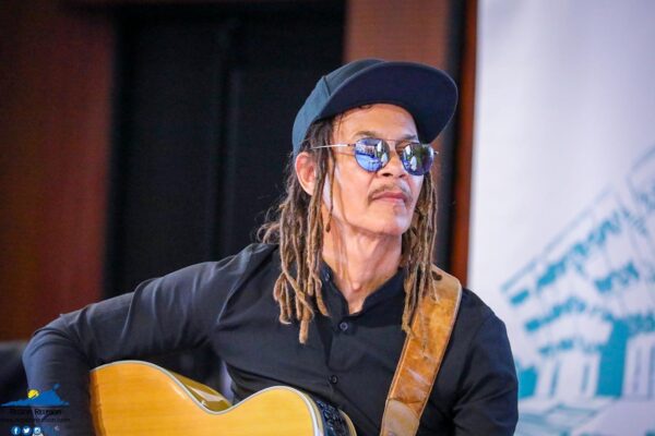 Thierry gauliris jouant de la guitare, portant des lunettes de soleil et une casquette.