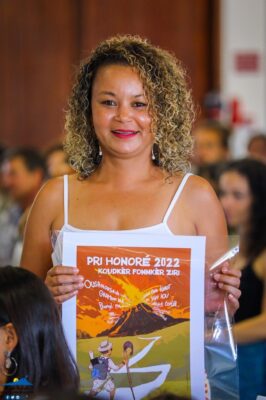 Une femme souriante tenant une affiche du Pri Honoré 2022.