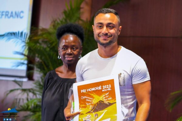 Un homme tenant une affiche du Pri Honoré 2022, accompagné d'une femme sur scène.