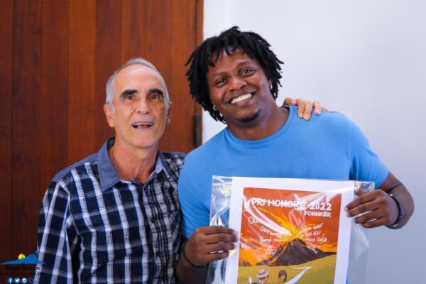 Deux hommes souriants posent ensemble, l'un tenant une affiche du Pri Honoré 2022.