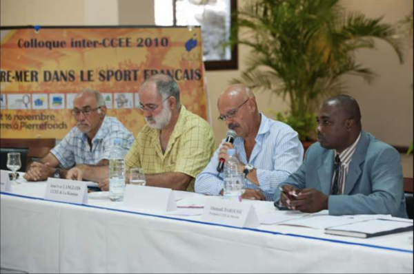Des intervenants assis à une table lors du colloque inter-CCEE 2010, avec l’un d’eux s’exprimant au micro.