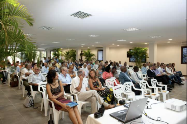 Une salle remplie de participants assis sur des chaises blanches lors d'une conférence.