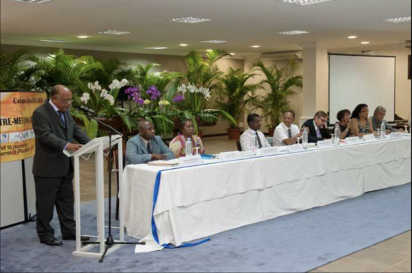 Une conférence avec des intervenants assis à une table, devant un décor de plantes.