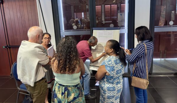 Un groupe de personnes participe à un atelier collaboratif. Un homme écrit des idées sur un tableau papier pendant que les autres échangent autour de lui