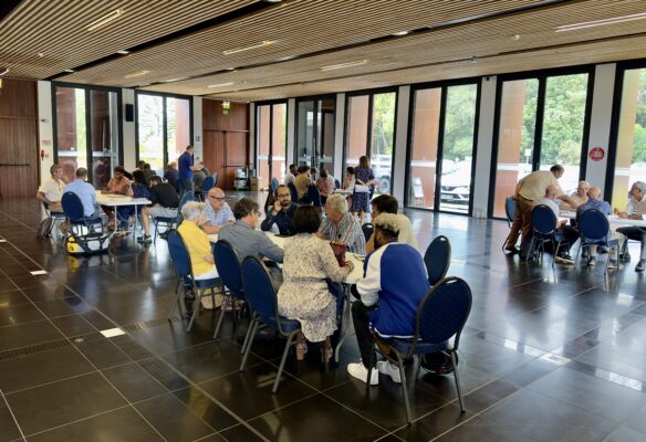 Plusieurs groupes de personnes sont assis autour de tables rondes dans une grande salle bien éclairée, participant à une activité collaborative ou un atelier.