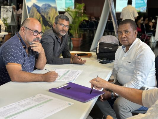 uatre hommes participent à un atelier collaboratif, prenant des notes sur des documents liés à la biodiversité. Ils sont assis autour d'une table avec des stylos en main et des documents devant eux