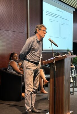 Gille lajoie membre du ccee se tient à un podium et présente lors d'un atelier sur la gestion de l'eau face au changement climatique. En arrière-plan, une présentation projetée sur un écran affiche des questions liées à la gestion de l'eau.
