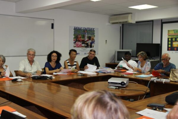 Participants lors d'une réunion du CCEE, assis autour d'une table en bois, avec des documents et un vidéoprojecteur posés sur la table.