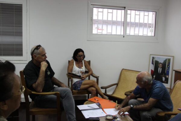 Discussion entre membres du CCEE dans une salle, avec des documents posés sur une table et un portrait officiel du président de la République visible en arrière-plan.