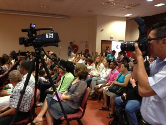 Une vue de l’audience pendant la remise des prix LanKRéol 2013 avec un cadreur filmant la scène et un photographe prenant des clichés. Les spectateurs sont assis attentivement, et certains prennent des notes