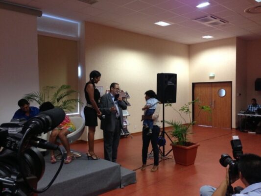 Un intervenant en costume remet un prix à une lauréate sur scène lors de la remise des prix LanKRéol 2013. Une caméra filme la scène au premier plan, et des spectateurs observent depuis la salle