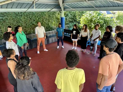 Un groupe de personnes debout en cercle à l'extérieur, participant à une activité ou discussion sous un abri.