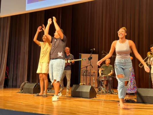 Groupe de personnes dansant joyeusement sur scène avec un groupe musical en arrière-plan.