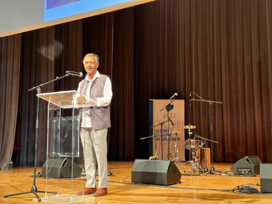 Discours de Roger Ramchetty , debout derrière un podium sur scène.