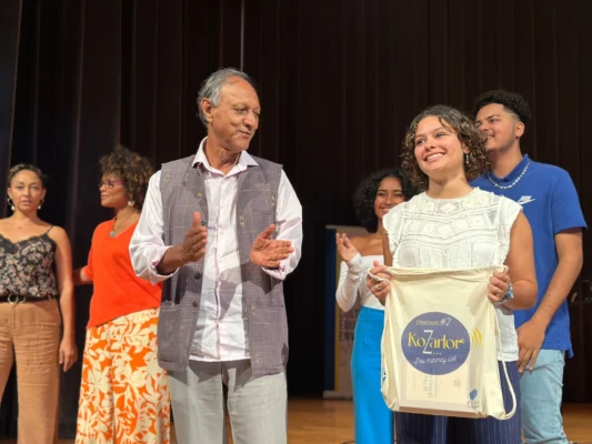 Lélia Jacque sourit avec son prix en main tandis que Roger Ramchetty applaudit à ses côtés.
