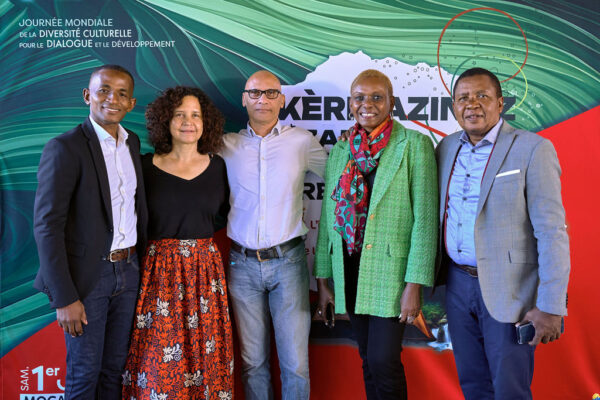 Photo de cinq personnes souriantes debout devant un fond avec le texte "Journée Mondiale de la Diversité Culturelle pour le Dialogue et le Développement