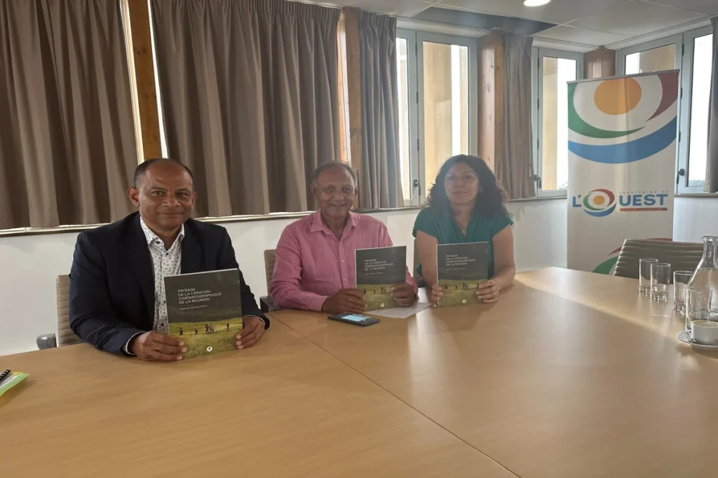 Elsa Dahamni, Roger RAmchetty et une autre personne posent avec un livre sur l'aménagement du paysage de La Réunion, dans une salle de réunion avec un logo de la région Ouest en arrière-plan.