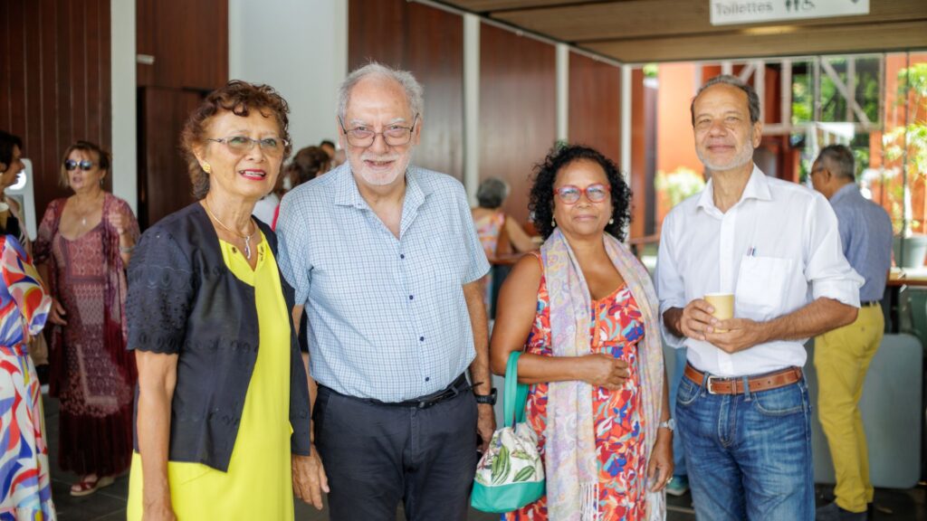Photo de quatre personnes posant lors de l'événement des 40 ans du CCEE : une femme en robe jaune et veste noire, un homme en chemise à carreaux, une femme en robe fleurie avec un châle, et un homme en chemise blanche avec un gobelet en main