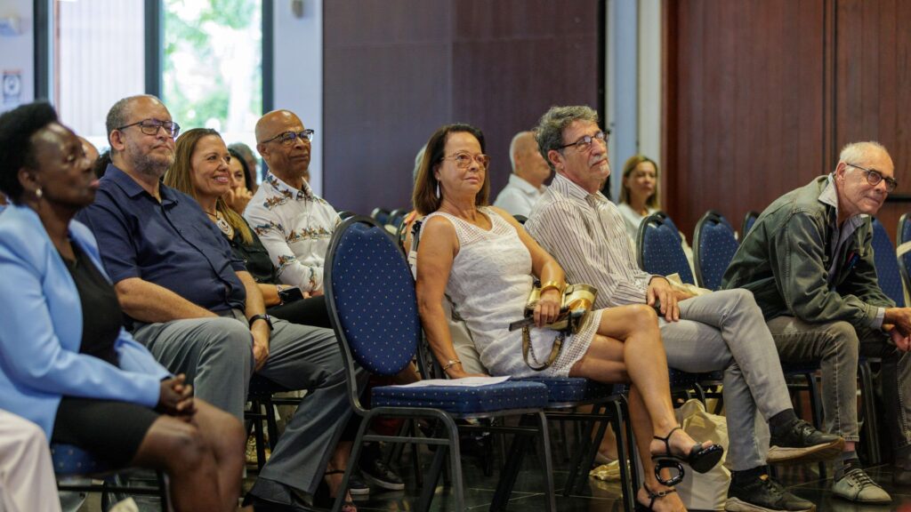 Des invités assis sur des chaises bleues lors des 40 ans du CCEE, parmi eux, Patricia Profil en veste bleue et plusieurs personnalités aux tenues variées écoutant l'intervention.