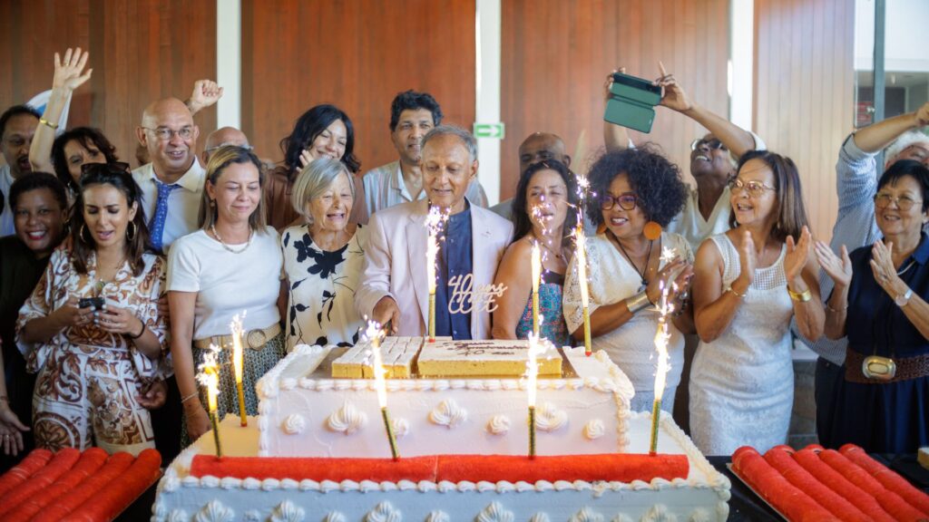Photo du personnel du CCEE célébrant les 40 ans autour d’un grand gâteau décoré de fontaines scintillantes. Roger Ramchetty, président du CCEE, coupe le gâteau, entouré de collègues applaudissant avec enthousiasme dans une ambiance festive