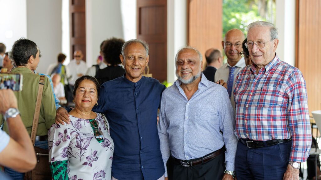 Photo de groupe avec trois hommes dont Roger Ramchetty le Président du CCEE et une femme posant ensemble, entourés de participants en arrière-plan dans un espace de réception décoré en bois lors des 40 ans du CCEE.