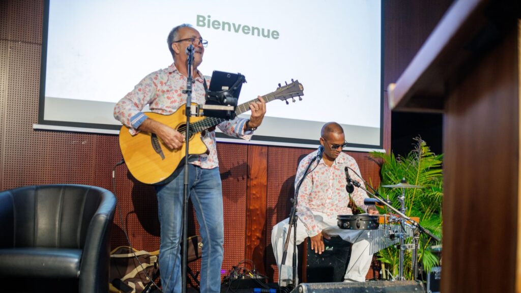 Photo de groupe avec trois hommes et une femme posant ensemble, entourés de participants en arrière-plan dans un espace de réception décoré en bois lors des 40 ans du CCEE.