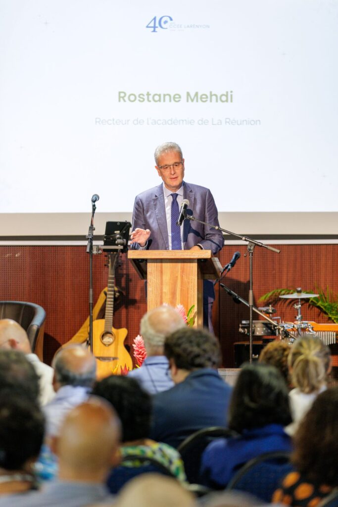 Rostane Mehdi, vêtu d'un costume bleu et d'une cravate à pois, s’exprimant derrière un pupitre en bois, avec un écran projetant son nom et sa fonction, lors de l’événement des 40 ans du CCEE.