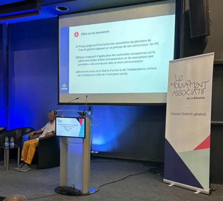 Présentation d’un intervenant sur les effets des politiques sur les associations, avec un pupitre et un écran de projection