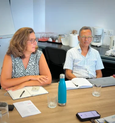 Un homme et une femme en discussion pendant la réunion du CESE et du CCEE, avec des carnets et ordinateurs sur la table