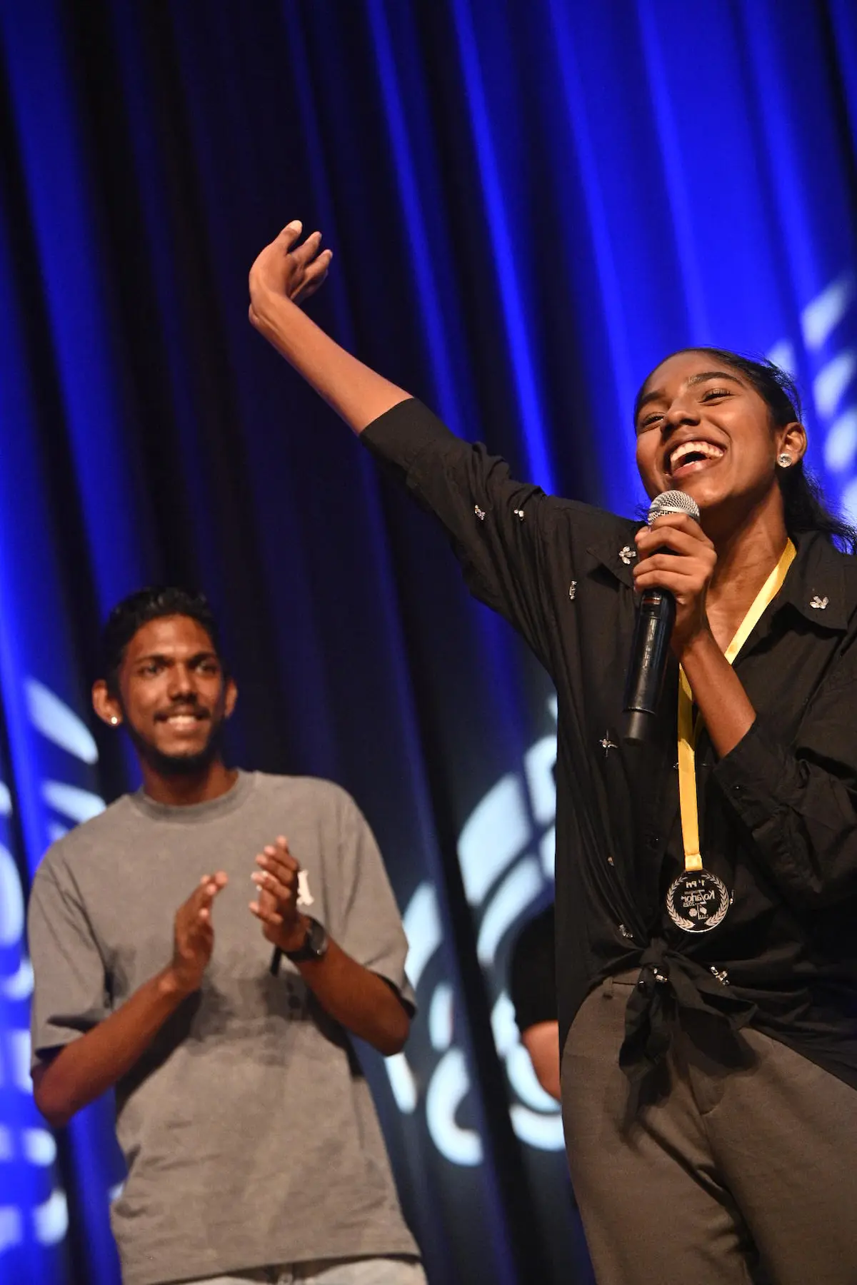 Cécile Crayer lève le bras et sourit sur scène avec sa médaille KoZarlor, sous les applaudissements d’un autre finaliste