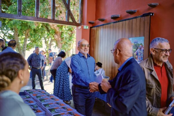 Accueil des participants à l'événement, avec poignées de main et distribution de brochures sur une table.