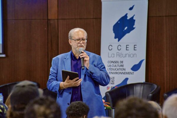 Dominique Picardo en costume bleu s’adressant au public, micro à la main, devant le kakémono du CCEE.