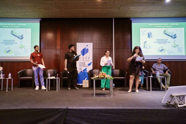 Groupe de jeunes présentant une idée sur la gestion des déchets, debout sur scène avec un support visuel projeté