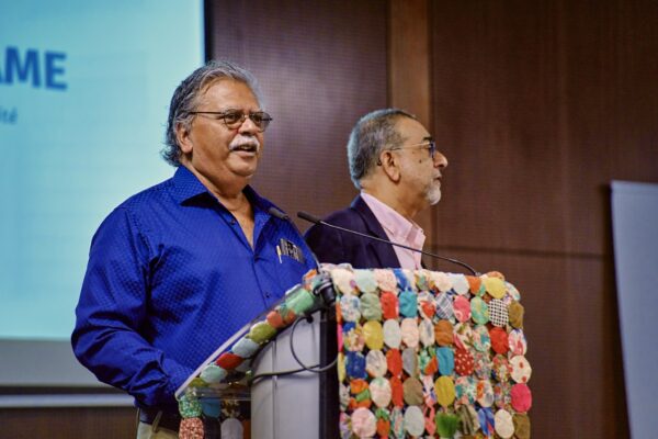 Deux hommes s’expriment à un pupitre orné d’un tissu coloré en patchwork, lors d’un événement du CCEE.