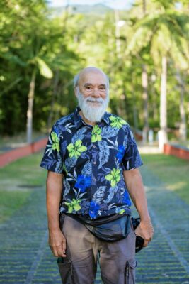 Portrait en extérieur d’un homme barbu souriant en chemise à fleurs, dans un cadre verdoyant