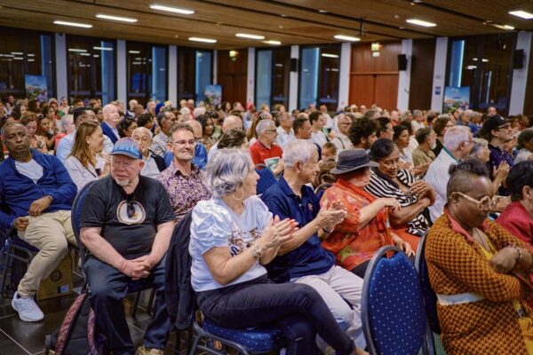 Vue latérale du public dans la salle de conférence, certaines personnes applaudissent.