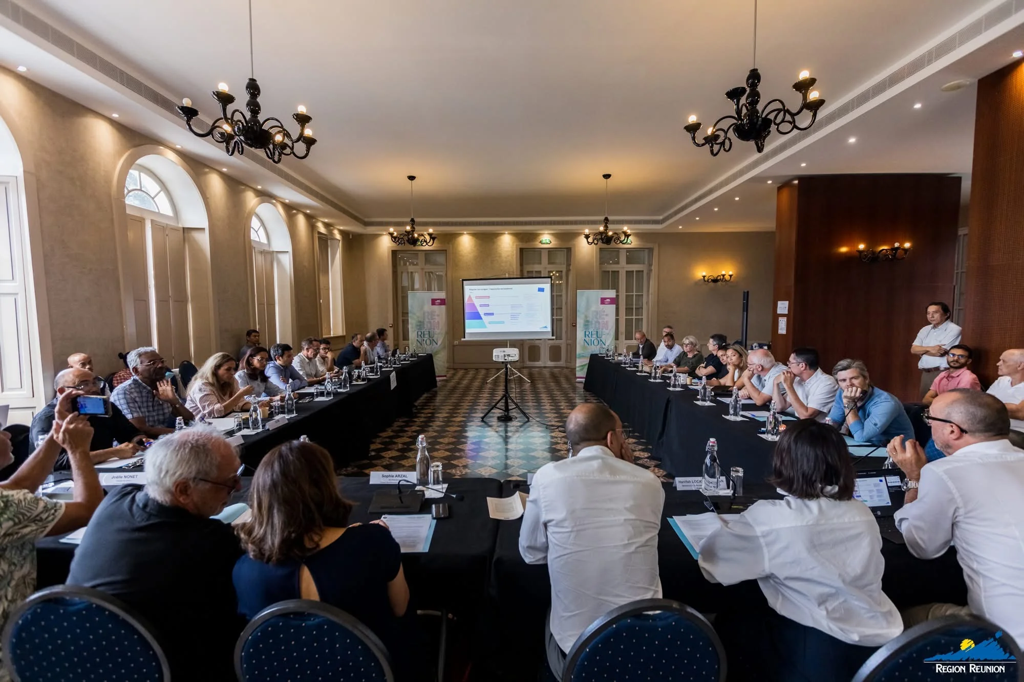 Vue d’ensemble de la réunion du Comité régional de la donnée et de l’IA, avec les participants installés autour de deux grandes tables en U.