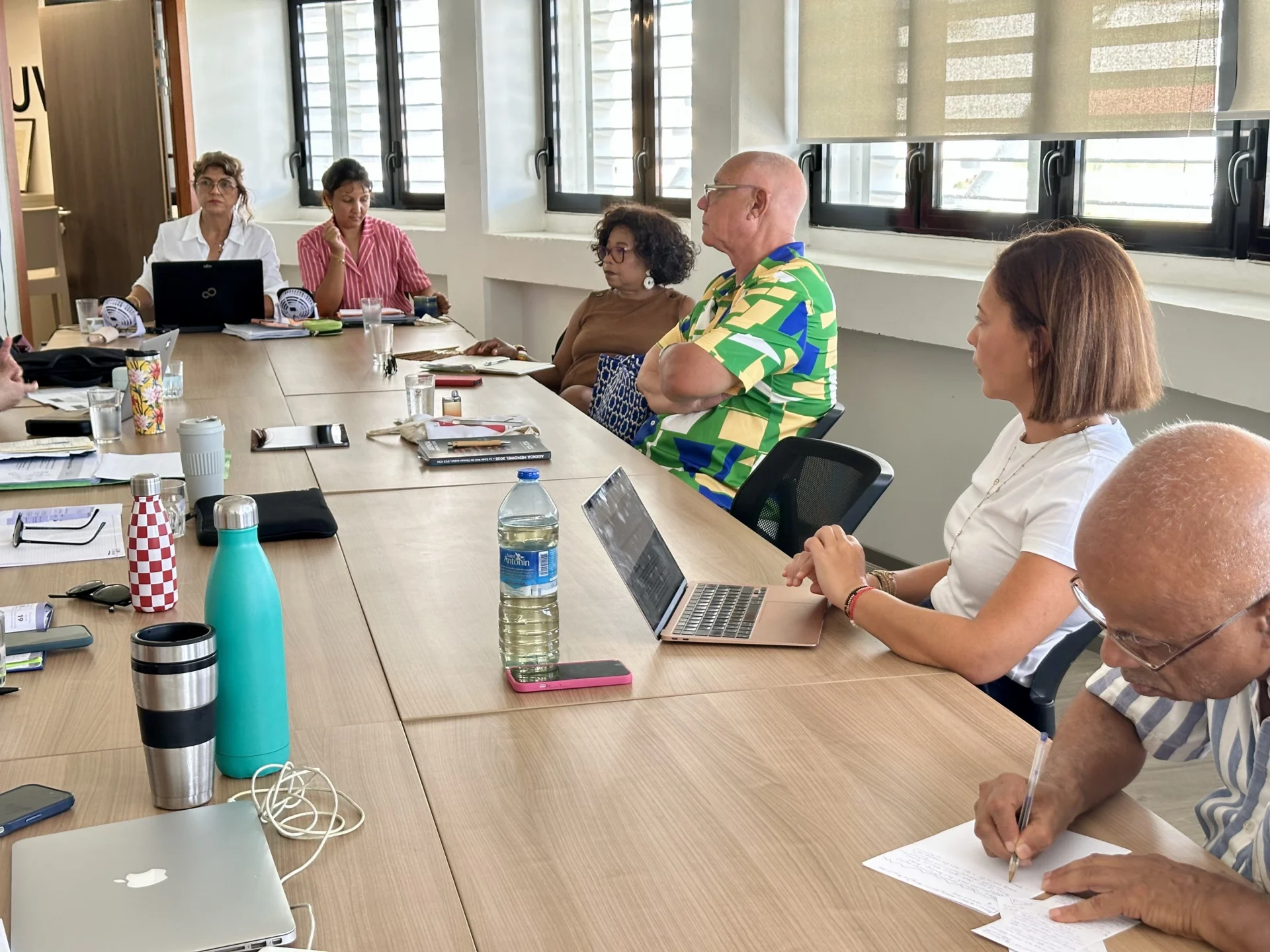 Vue d'ensemble d'une table de réunion avec plusieurs participants concentrés, utilisant des ordinateurs portables.
