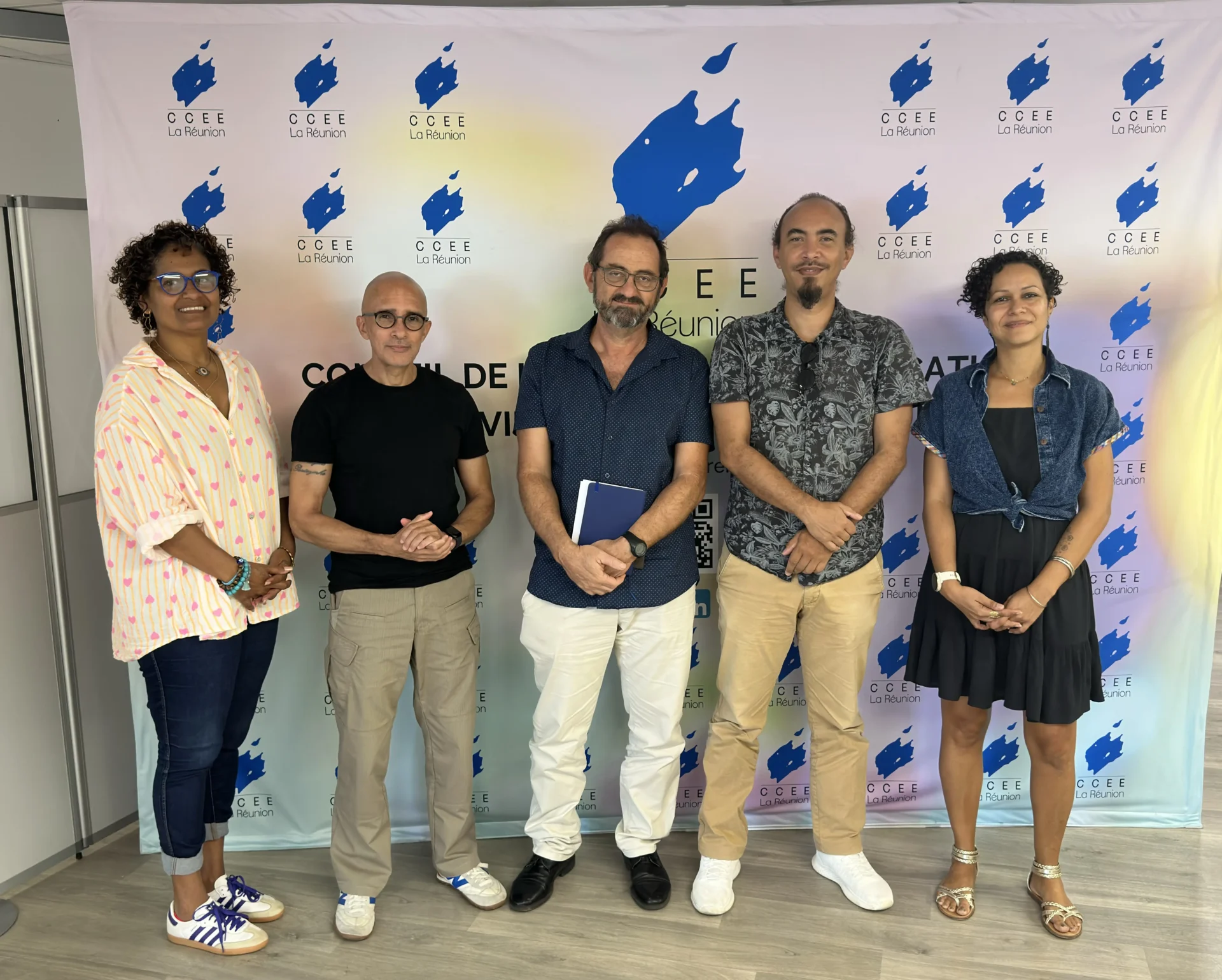 Photo du jury composé de cinq personnes (deux femmes et trois hommes) posant debout devant un photocall blanc orné du logo bleu du CCEE La Réunion. Ils sont habillés de manière décontractée et sourient face à l'objectif.