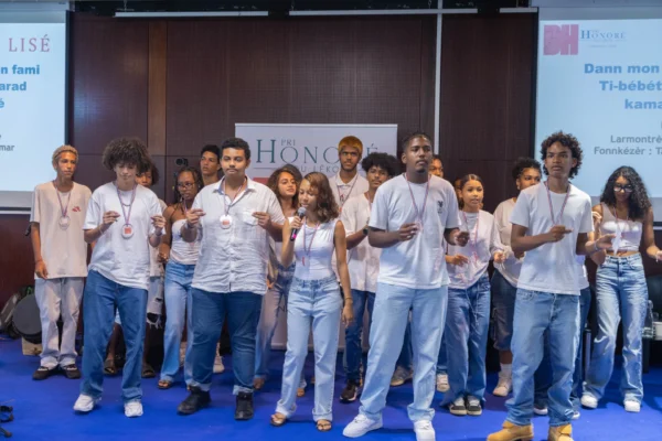 Groupe d’élèves sur scène lors d’une prestation collective dans le cadre du Pri Honoré pou lékol 2026. Une participante tient un microphone au centre du groupe.