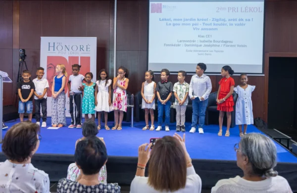 Des élèves se tiennent sur scène lors d’une remise de prix du Pri Honoré pou lékol 2026, devant le public.