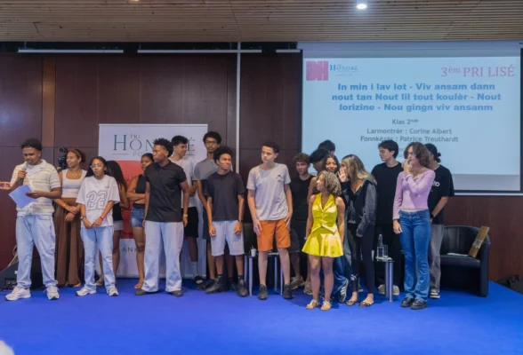 Groupe de lycéens réunis sur scène lors du Pri Honoré pou lékol 2026, devant un écran de projection présentant une œuvre récompensée.